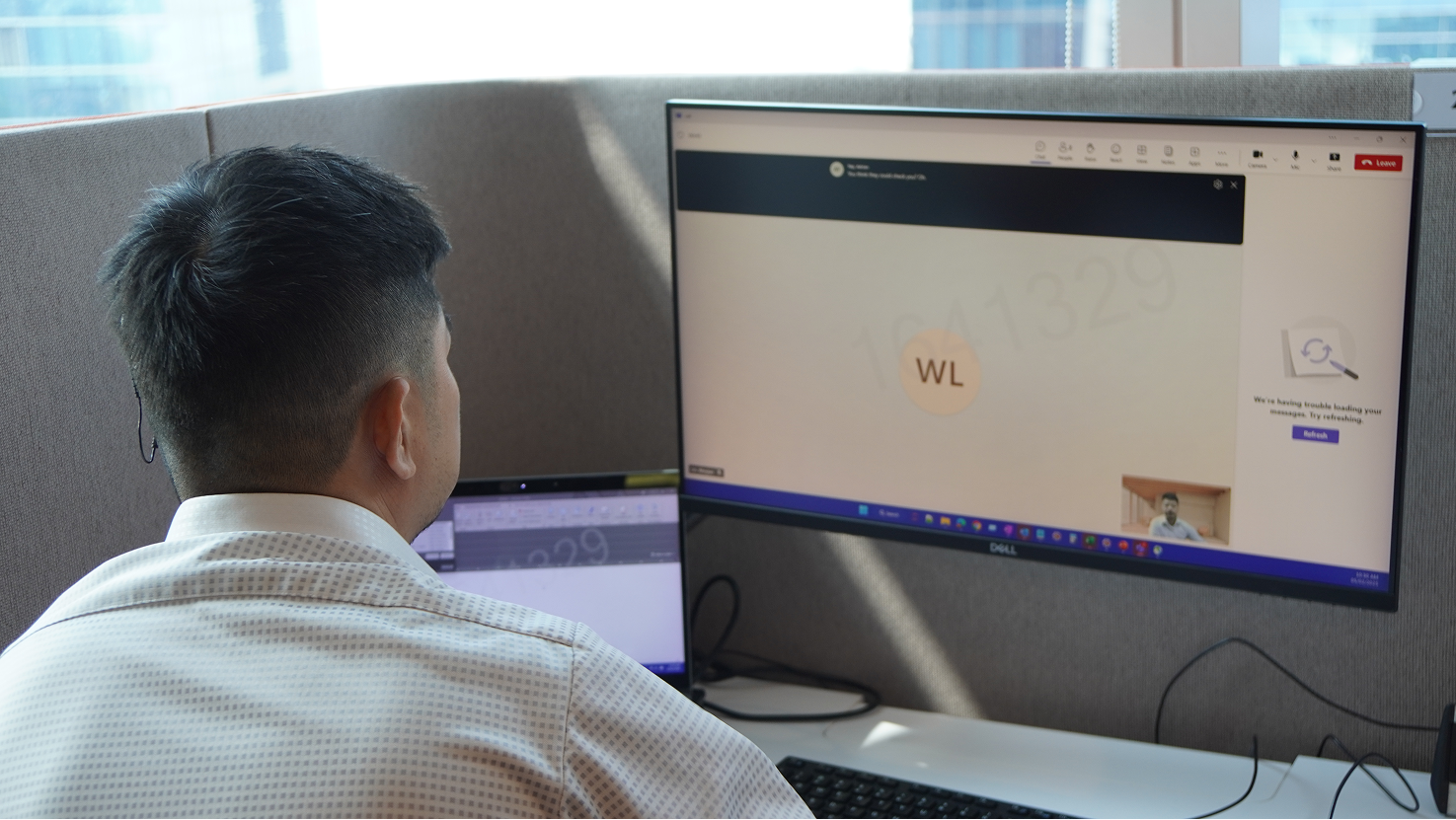 Person at desk facing Dell monitors, one showing a Microsoft Teams error message.